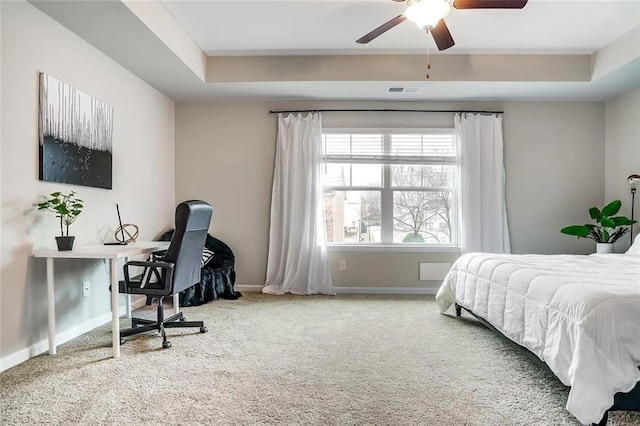 carpeted bedroom featuring a raised ceiling, a ceiling fan, and baseboards