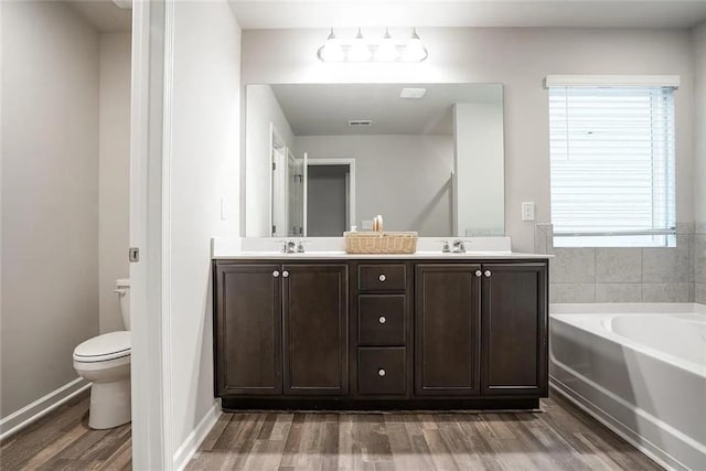 full bathroom with wood finished floors, double vanity, a sink, a garden tub, and toilet