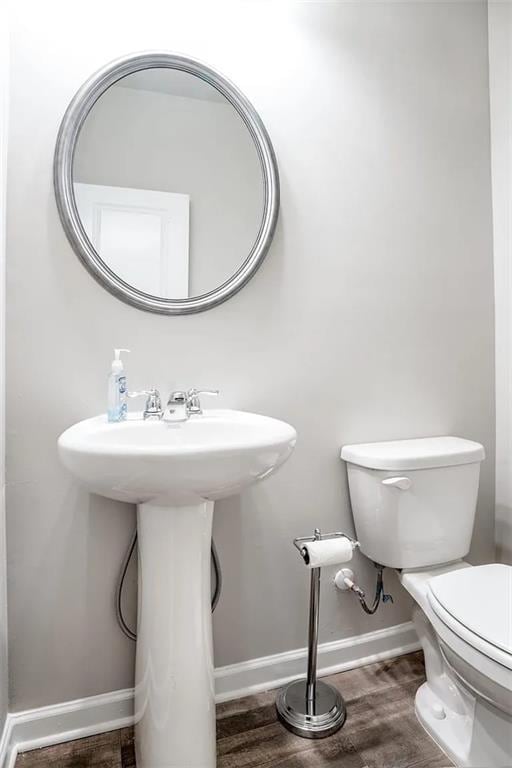 half bathroom with a sink, toilet, baseboards, and wood finished floors