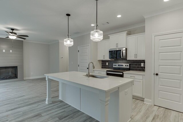 kitchen with white cabinetry, stainless steel appliances, hanging light fixtures, and an island with sink