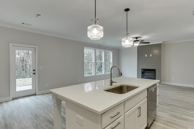 kitchen featuring a large fireplace, sink, dishwasher, white cabinetry, and an island with sink