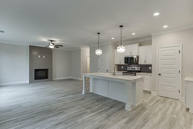 kitchen with white cabinetry, sink, stainless steel appliances, a kitchen island with sink, and light wood-type flooring