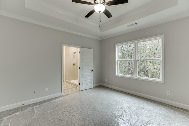 unfurnished bedroom with a tray ceiling, ensuite bath, and ceiling fan