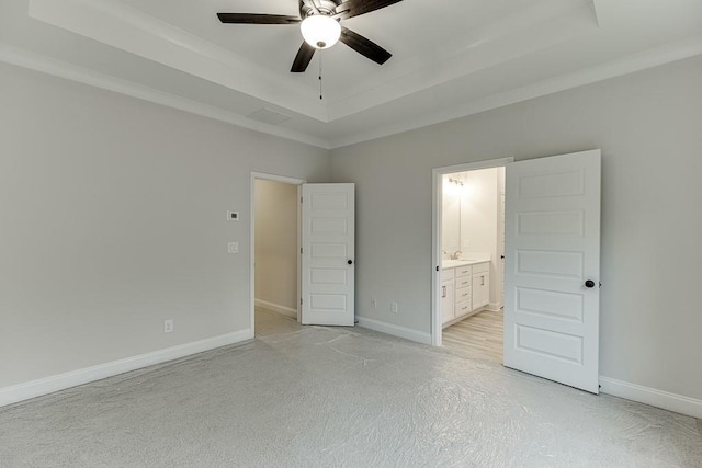 unfurnished bedroom with ceiling fan, a raised ceiling, light colored carpet, and ensuite bathroom