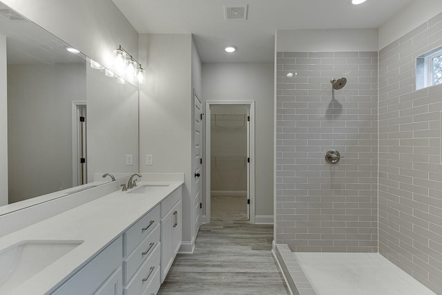 bathroom with wood-type flooring, vanity, and a tile shower