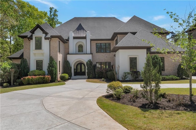 french country inspired facade featuring french doors, curved driveway, roof with shingles, and stucco siding