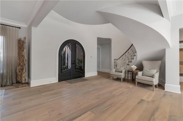 foyer featuring arched walkways, french doors, stairway, light wood finished floors, and baseboards