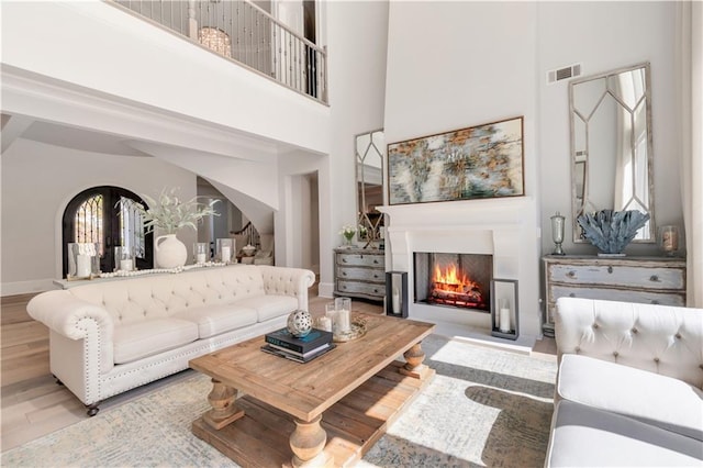 living room with a high ceiling, a lit fireplace, wood finished floors, and baseboards