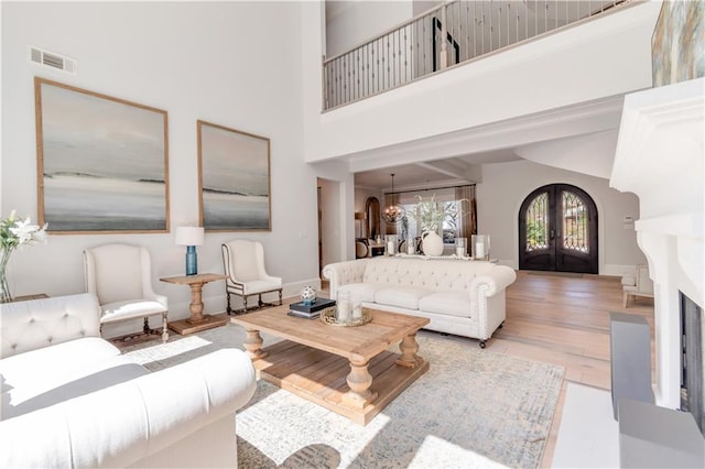 living area featuring light wood-type flooring, a towering ceiling, french doors, and a chandelier
