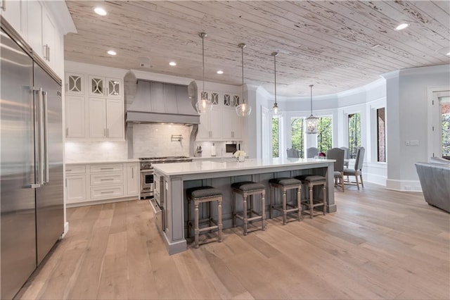 kitchen with premium appliances, custom exhaust hood, light wood-style flooring, crown molding, and white cabinetry