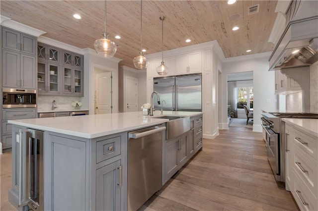 kitchen featuring high end appliances, gray cabinetry, wooden ceiling, a center island with sink, and light countertops