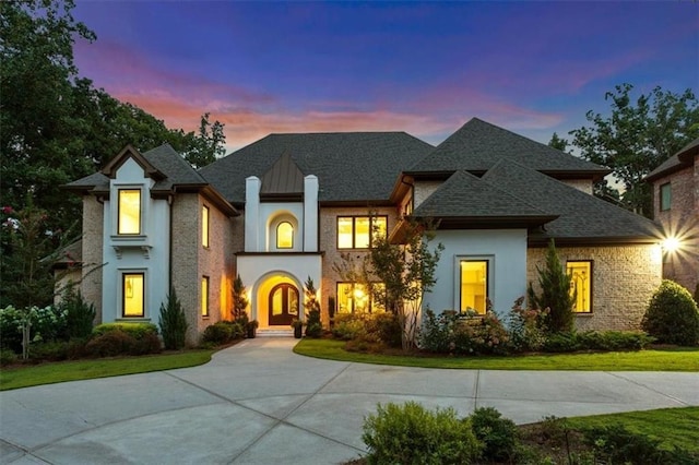 french country home featuring a front yard, a shingled roof, and stucco siding