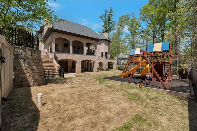 rear view of property with stairs, a playground, a chimney, and brick siding