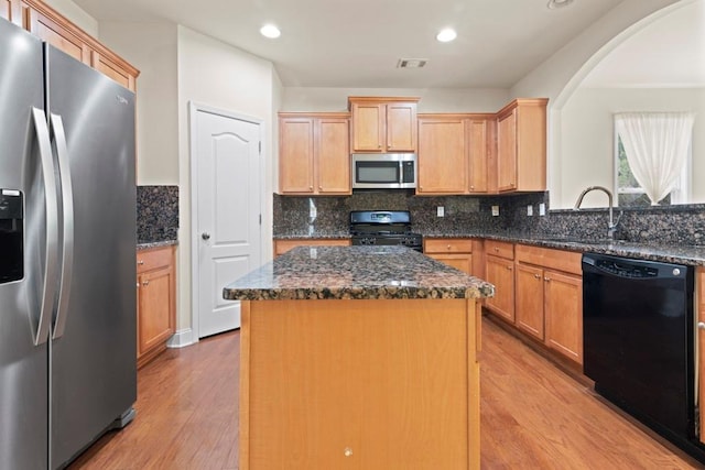 kitchen featuring a sink, visible vents, light wood-type flooring, a center island, and black appliances