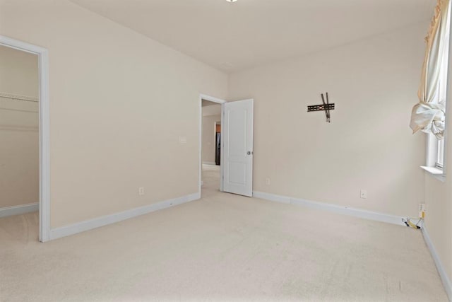 unfurnished bedroom with light carpet, baseboards, a walk in closet, and a closet