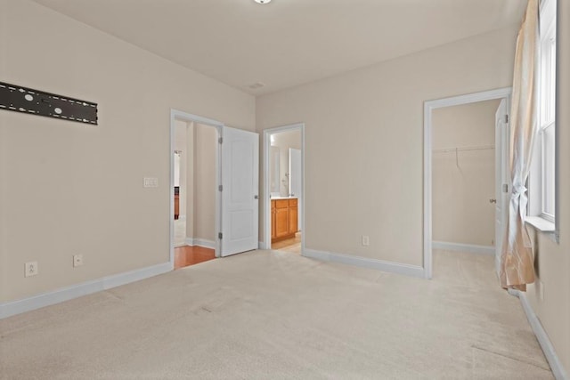 unfurnished bedroom featuring baseboards, a walk in closet, and light colored carpet