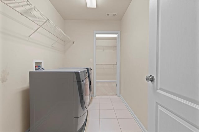 clothes washing area with washing machine and clothes dryer, light tile patterned floors, visible vents, laundry area, and baseboards