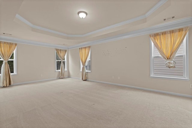 carpeted spare room with ornamental molding, a tray ceiling, visible vents, and baseboards