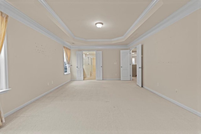 empty room with ornamental molding, a tray ceiling, baseboards, and light colored carpet