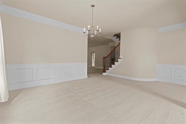 spare room featuring stairway, an inviting chandelier, carpet, crown molding, and a decorative wall