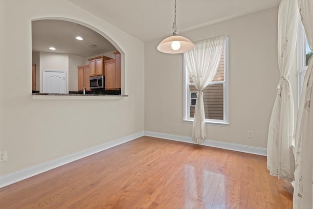 unfurnished dining area with arched walkways, light wood-style flooring, baseboards, and recessed lighting