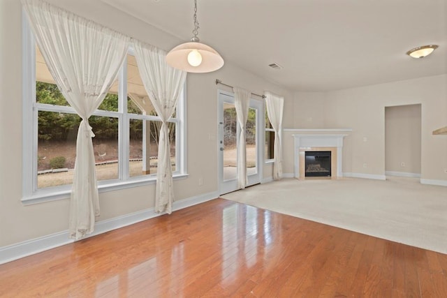 unfurnished living room with baseboards, visible vents, wood finished floors, and a glass covered fireplace