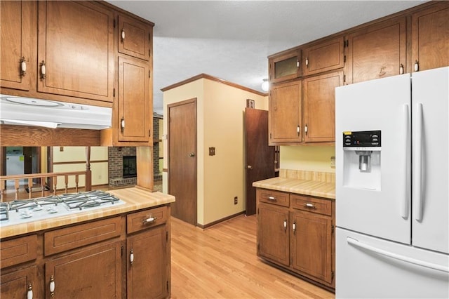 3802 SW Knights Bridge Rd SW, Lilburn, GA 30047 - kitchen featuring white appliances, light wood-style flooring, under cabinet range hood, brown cabinets, and ornamental molding