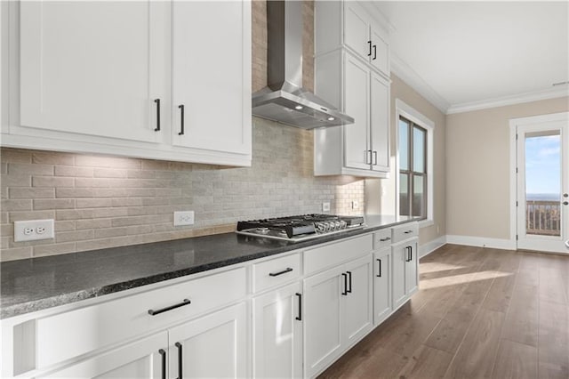 kitchen featuring decorative backsplash, ornamental molding, dark wood-style flooring, wall chimney range hood, and stainless steel gas stovetop