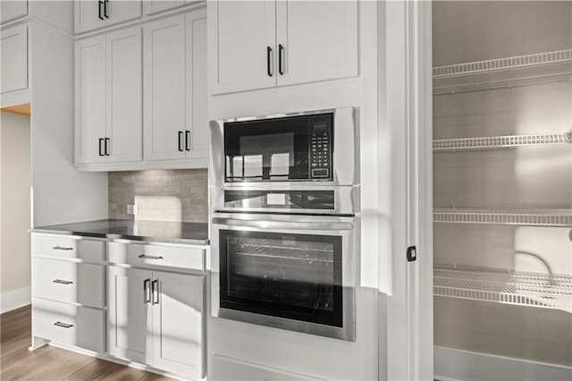 kitchen with black microwave, wood finished floors, stainless steel oven, baseboards, and decorative backsplash