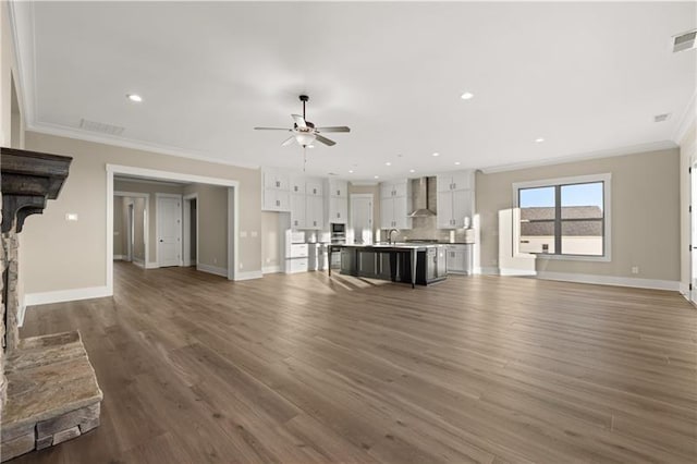 unfurnished living room with visible vents, ornamental molding, ceiling fan, a sink, and wood finished floors