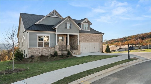 craftsman house featuring driveway, stone siding, metal roof, a standing seam roof, and a front lawn