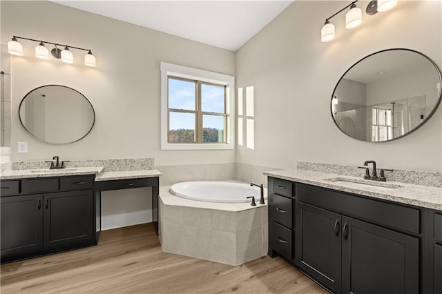 full bathroom featuring two vanities, a sink, a bath, and wood finished floors