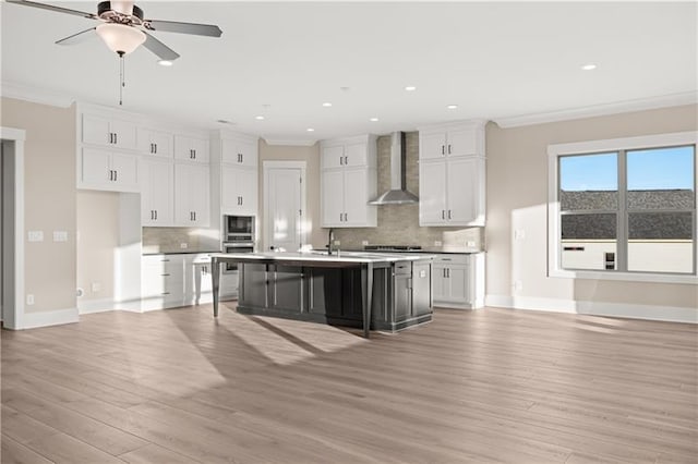 kitchen featuring light wood-type flooring, wall chimney exhaust hood, ornamental molding, and white cabinets