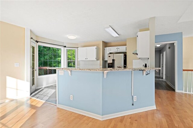 kitchen featuring light wood finished floors, a kitchen breakfast bar, white cabinets, and stainless steel fridge with ice dispenser