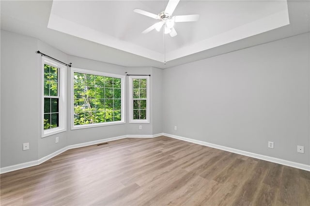 spare room featuring visible vents, wood finished floors, baseboards, ceiling fan, and a tray ceiling