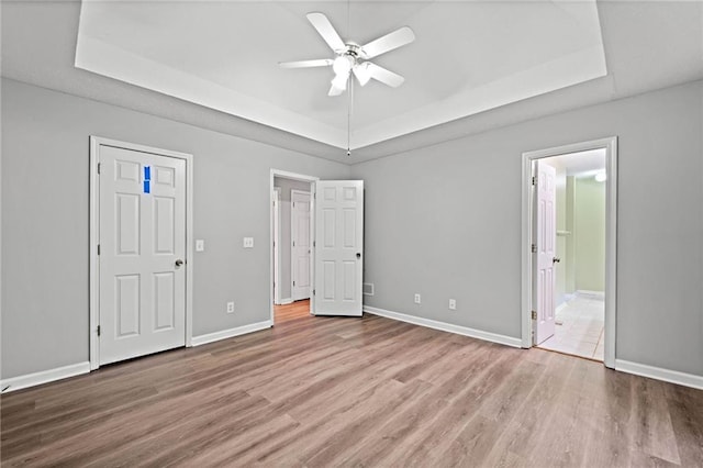 unfurnished bedroom with baseboards, connected bathroom, a raised ceiling, and wood finished floors