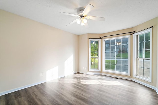 empty room with a ceiling fan, baseboards, plenty of natural light, and wood finished floors
