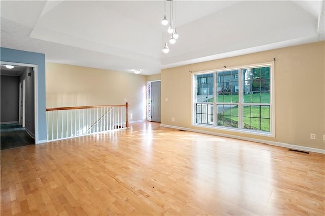 empty room with a raised ceiling, baseboards, wood finished floors, and visible vents