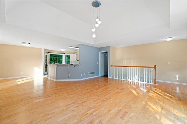 interior space with visible vents, a raised ceiling, light wood finished floors, and baseboards