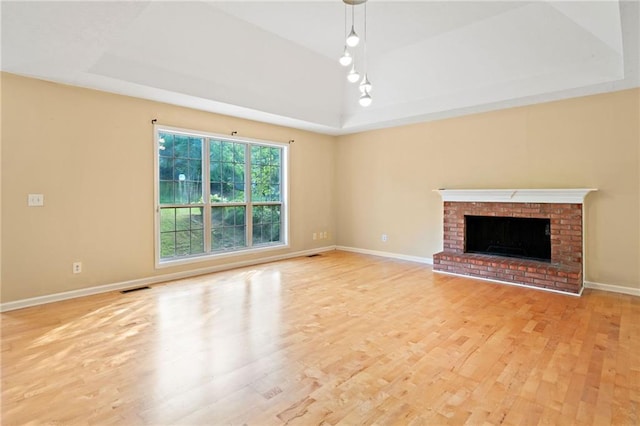 unfurnished living room with visible vents, a brick fireplace, light wood-type flooring, a raised ceiling, and baseboards