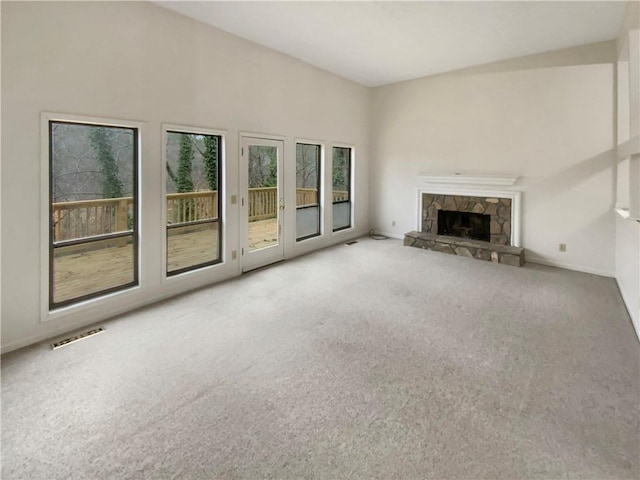 unfurnished living room featuring a stone fireplace and carpet floors