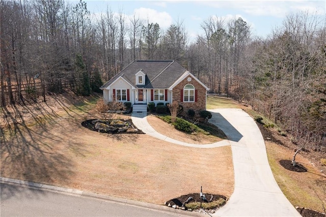 view of front of property with driveway, a forest view, and a front lawn