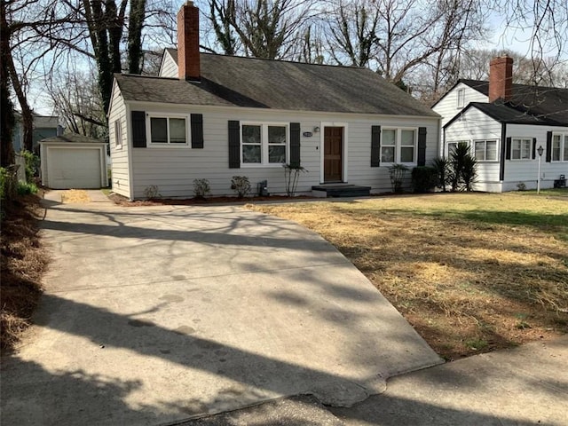 cape cod home featuring an outbuilding, a detached garage, concrete driveway, a front yard, and a chimney