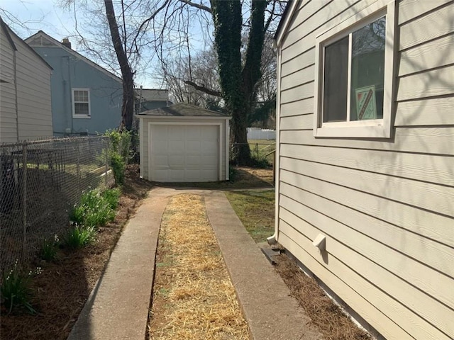 view of side of home with concrete driveway, an outbuilding, fence, and a detached garage