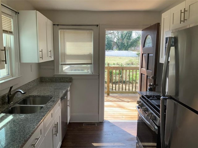 kitchen with appliances with stainless steel finishes, dark wood-style floors, white cabinets, stone countertops, and a sink