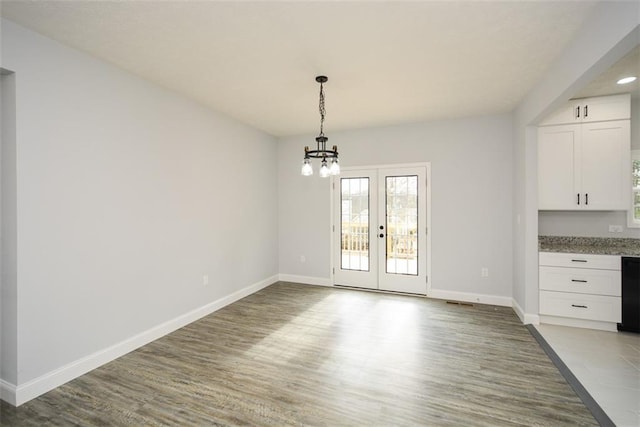 unfurnished dining area with hardwood / wood-style flooring, french doors, and a chandelier