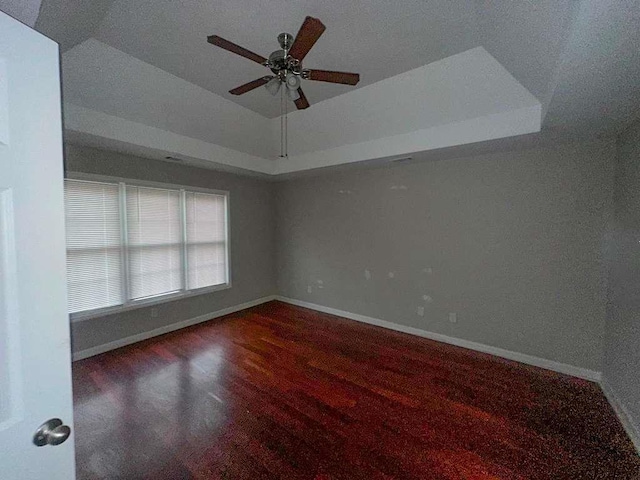 unfurnished room with wood finished floors, a tray ceiling, and baseboards
