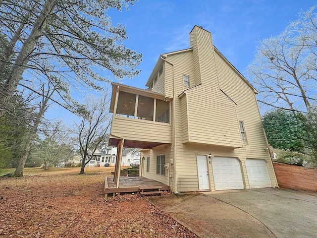 exterior space with a chimney, driveway, a sunroom, and an attached garage