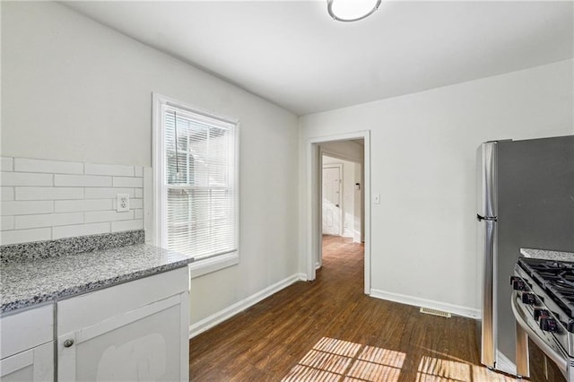 kitchen with stainless steel range with gas stovetop, tasteful backsplash, light stone countertops, white cabinets, and dark hardwood / wood-style flooring