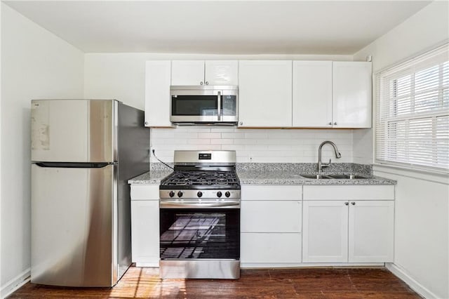 kitchen with appliances with stainless steel finishes, dark hardwood / wood-style floors, white cabinetry, sink, and backsplash